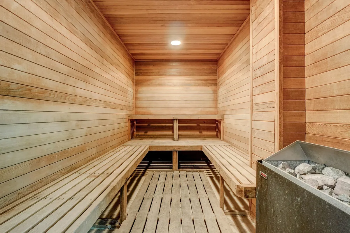 A tranquil sauna room featuring smooth wooden benches and walls, centered around a traditional sauna heater. The space exudes warmth and a sense of peaceful retreat.