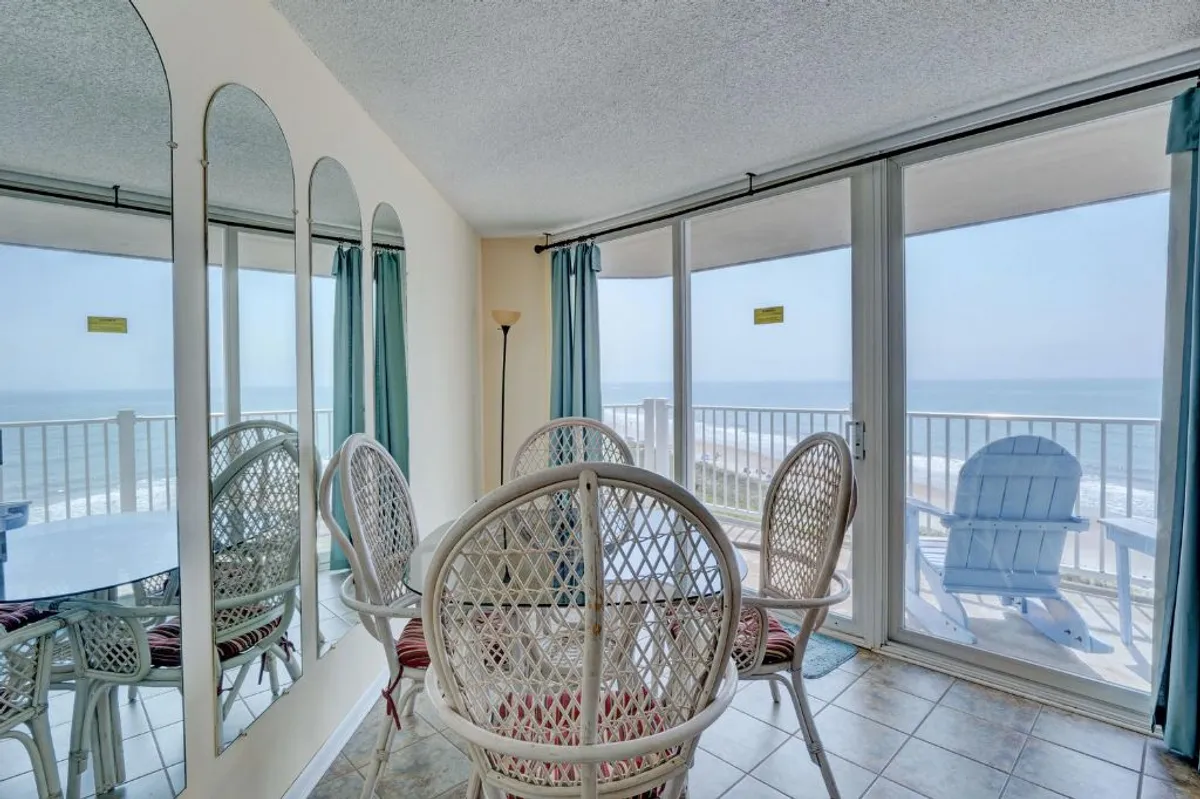 A cheerful dining area with a dining table, woven chairs, large windows for lots of natural light, mirrors, and an ocean view. The space feels bright and tranquil, ideal for shared meals or casual relaxation.