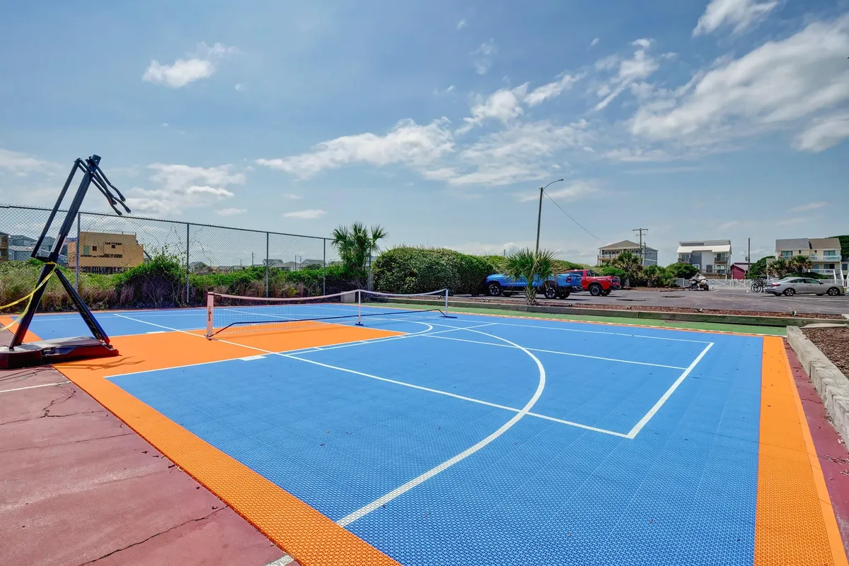 A vibrant multi-use sport court featuring a basketball hoop and tennis net, with a colorful court surface. The area is set up for active outdoor fun, perfect for games and friendly competitions under the sun.