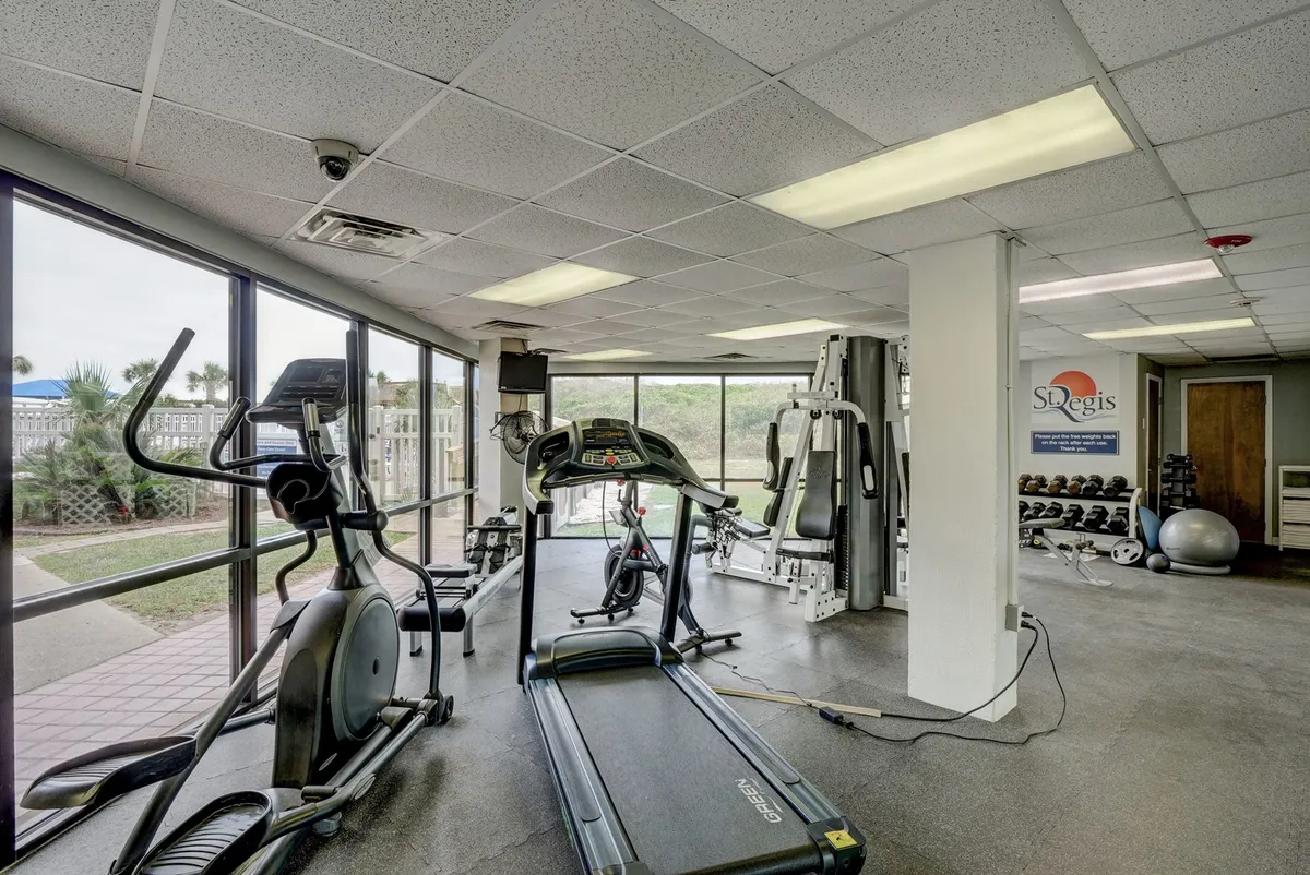 A modern fitness center with treadmills, elliptical machines, weight machines, and large windows letting in natural light. The setup is fresh and motivational, providing a glimpse of the active lifestyle options available to guests.