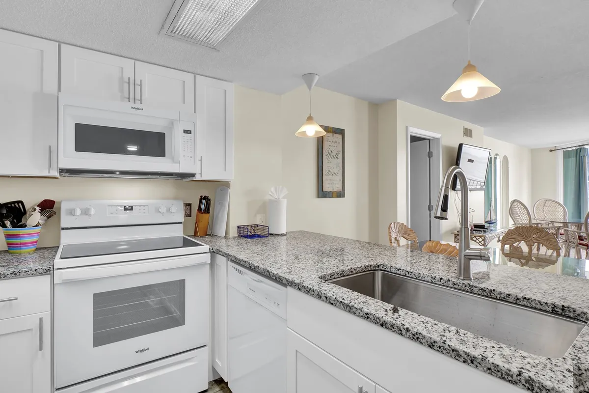 A close-up of the well-equipped kitchen with granite countertops, white cabinetry, modern appliances, and decorative wall art. The setting feels functional and welcoming, ready for preparing meals or hosting.