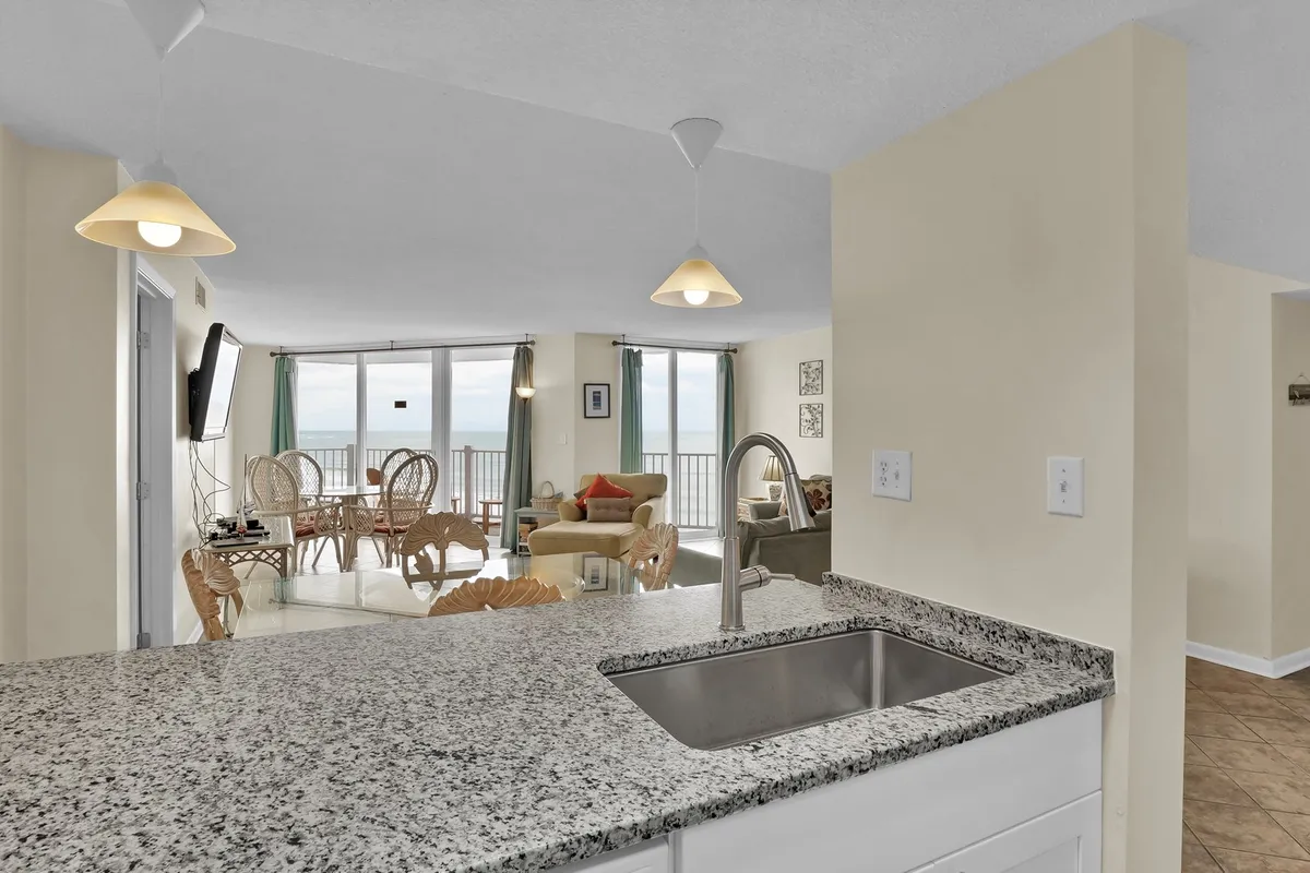 An inviting interior shot featuring a granite countertop, comfortable living area with seating, and large windows overlooking a scenic view. The setup suggests easy entertaining and enjoying meals with loved ones while staying connected to the natural beauty outside.