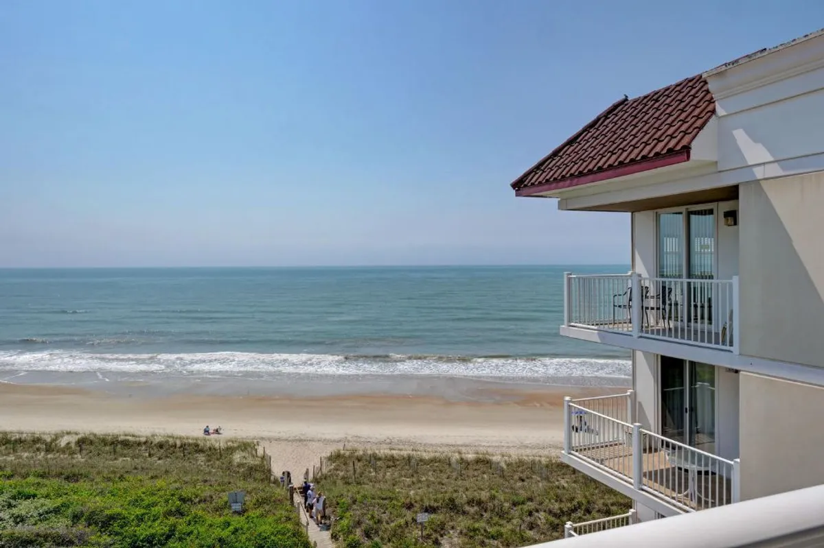This image displays a private balcony with a clear view of the ocean and sandy beach, with the building’s architecture framing the scene. The balcony setting visually connects the interior condo space to the outdoor coastal environment, ideal for morning coffee and relaxation.