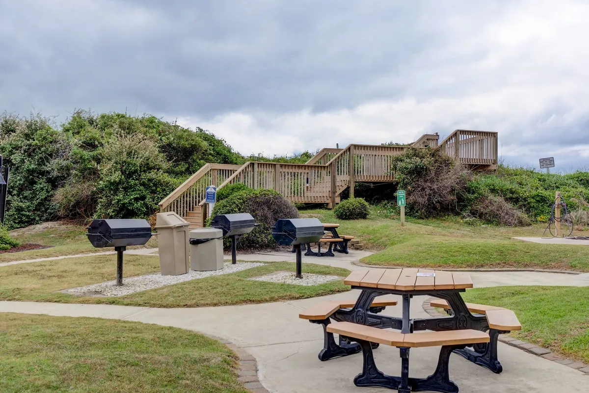 The photo features picnic tables and outdoor charcoal grills, set in a relaxed, communal atmosphere. The presence of grills and seating suggests spaces perfect for cookouts, barbecues, and gatherings with family or friends.